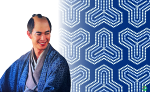 大河ドラマ『べらぼう』の田沼意知役の俳優と、背景に描かれた青い毘沙門亀甲文様のグラフィック。